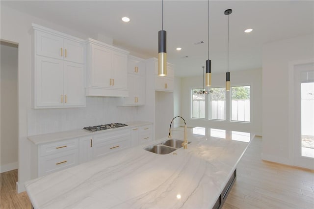 kitchen featuring stainless steel gas cooktop, sink, hanging light fixtures, light stone countertops, and white cabinets