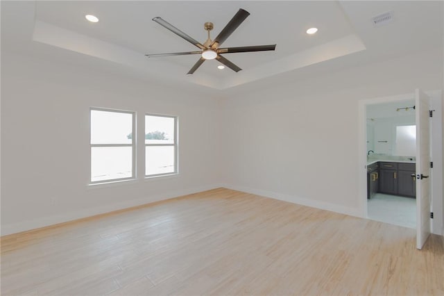 spare room featuring ceiling fan, a raised ceiling, and light wood-type flooring