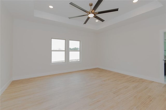 spare room featuring light hardwood / wood-style flooring, ceiling fan, and a tray ceiling