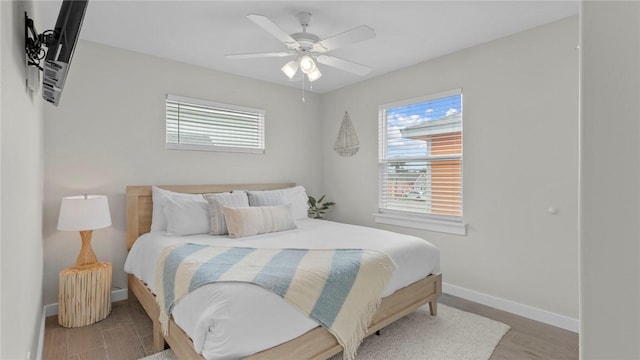 bedroom featuring multiple windows, ceiling fan, baseboards, and wood finished floors