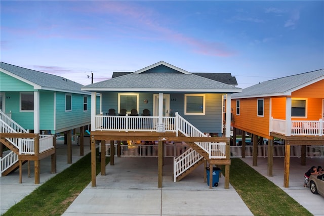 coastal inspired home with stairway, a porch, a carport, and roof with shingles