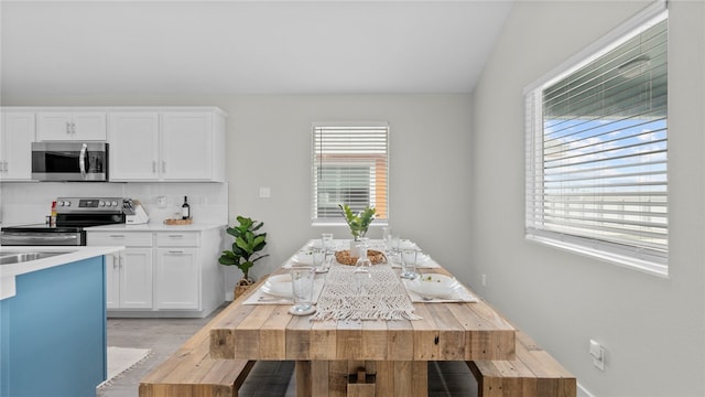 kitchen with stainless steel appliances, white cabinetry, vaulted ceiling, light hardwood / wood-style flooring, and decorative backsplash