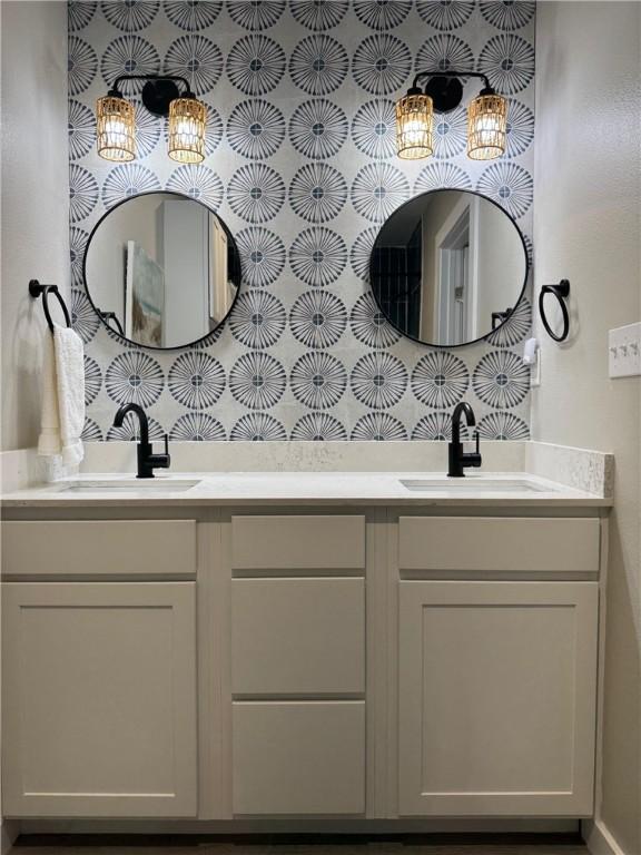 full bathroom featuring double vanity, wallpapered walls, and a sink