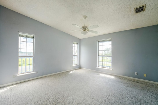 carpeted spare room featuring a healthy amount of sunlight, visible vents, vaulted ceiling, and a textured ceiling