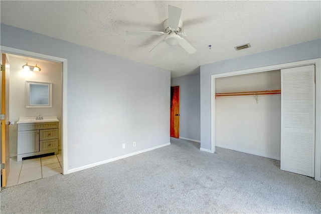 unfurnished bedroom with a closet, visible vents, light carpet, a sink, and a textured ceiling