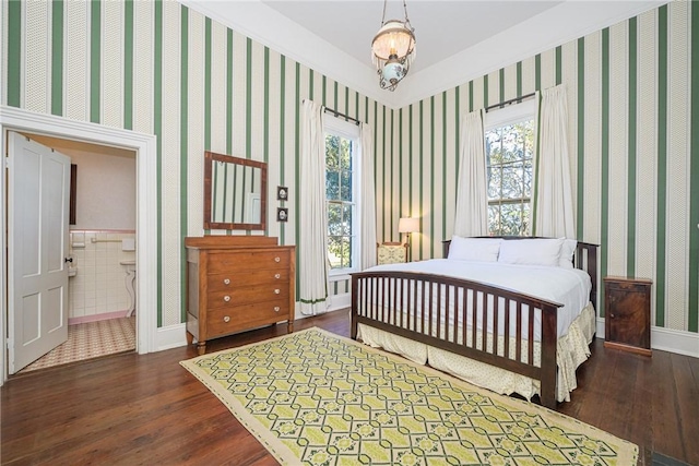 bedroom featuring connected bathroom, dark wood-type flooring, and a notable chandelier