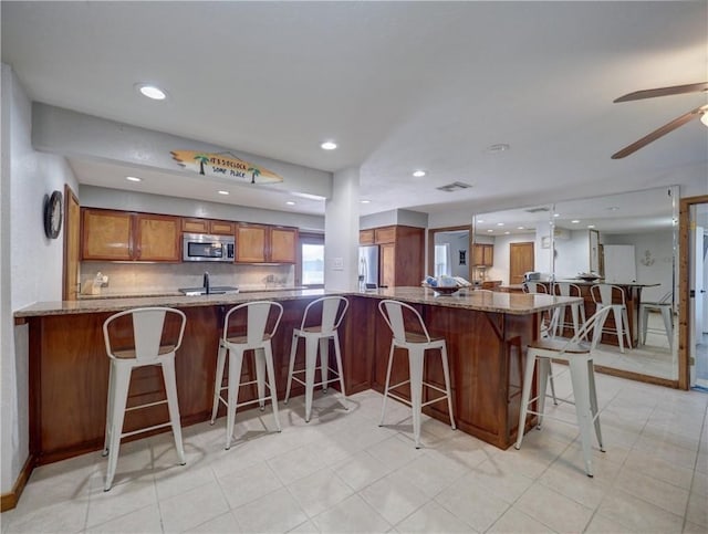 kitchen with stainless steel appliances, light stone counters, a kitchen bar, and kitchen peninsula