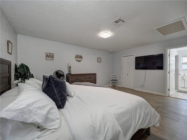 bedroom featuring ensuite bathroom, a textured ceiling, and light wood-type flooring