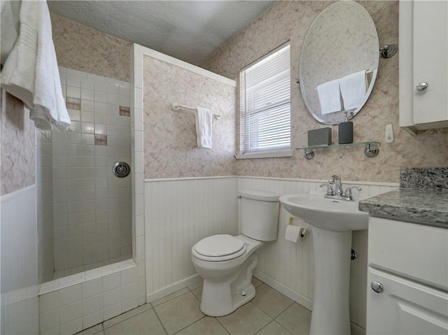 bathroom featuring tile patterned floors, toilet, sink, a textured ceiling, and a tile shower