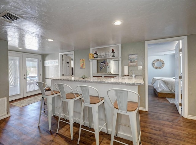 kitchen with sink, dark wood-type flooring, light stone counters, a textured ceiling, and french doors