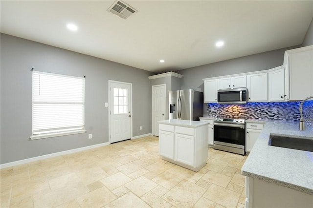 kitchen with sink, appliances with stainless steel finishes, tasteful backsplash, white cabinets, and a kitchen island