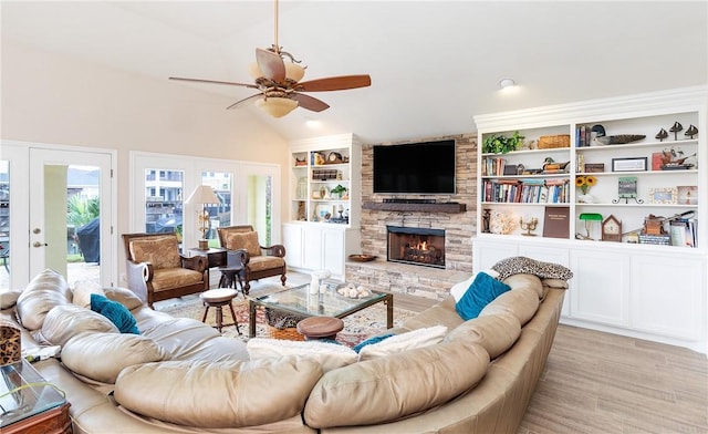 living room featuring ceiling fan, lofted ceiling, light hardwood / wood-style flooring, a stone fireplace, and french doors