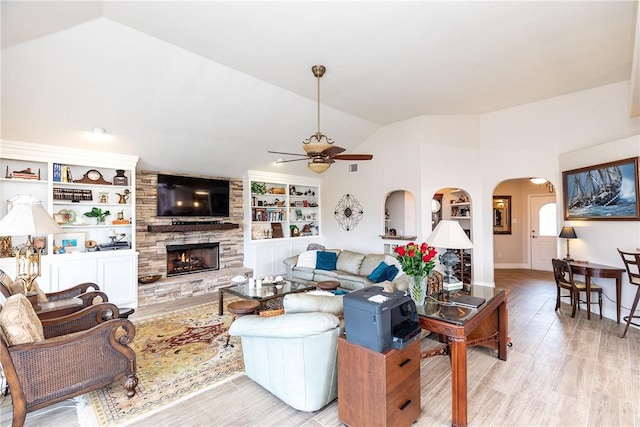 living room with ceiling fan, light wood-type flooring, a fireplace, built in features, and vaulted ceiling