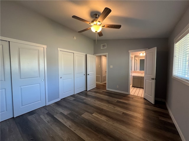 unfurnished bedroom featuring dark hardwood / wood-style flooring, two closets, vaulted ceiling, and ceiling fan