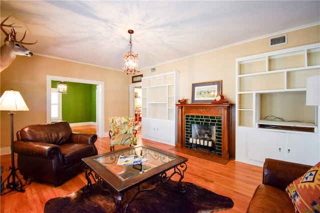 living room featuring an inviting chandelier, a tiled fireplace, light wood-type flooring, and ornamental molding