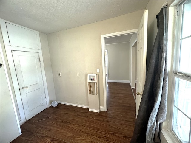 hall with a wealth of natural light, dark hardwood / wood-style flooring, and a textured ceiling