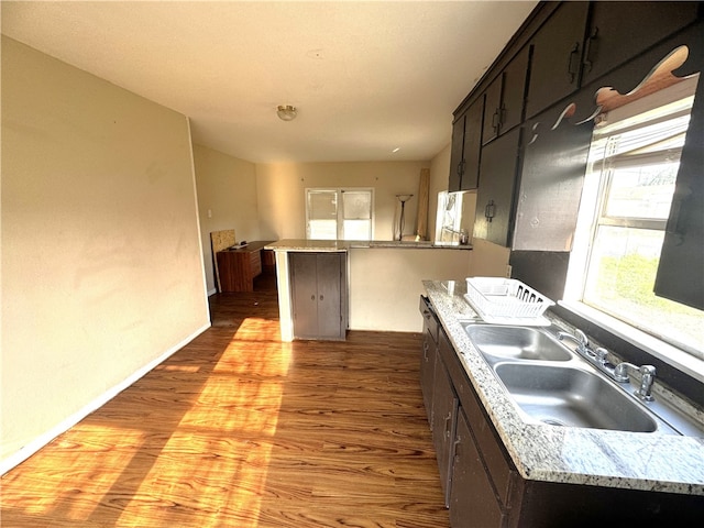 kitchen featuring dark brown cabinetry, light stone countertops, sink, light hardwood / wood-style floors, and a center island