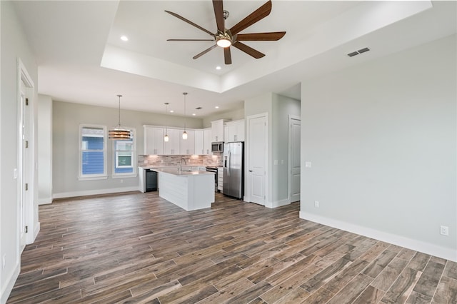 kitchen with stainless steel appliances, a center island with sink, white cabinetry, dark hardwood / wood-style floors, and pendant lighting