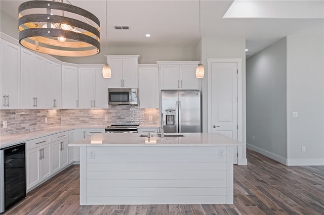 kitchen featuring white cabinets, stainless steel appliances, a kitchen island with sink, and beverage cooler