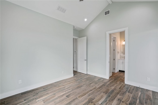 unfurnished bedroom with dark hardwood / wood-style flooring, high vaulted ceiling, and ensuite bath