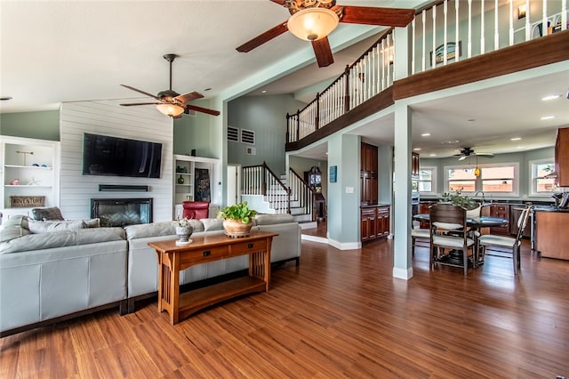 living room with dark hardwood / wood-style flooring, ceiling fan, high vaulted ceiling, and a large fireplace