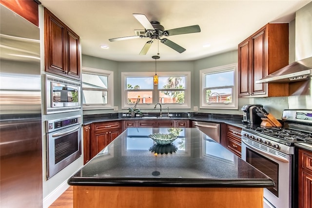 kitchen featuring built in appliances, wall chimney exhaust hood, sink, a kitchen island, and light wood-type flooring