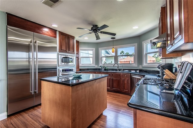 kitchen with dark hardwood / wood-style flooring, ceiling fan, built in appliances, and a center island