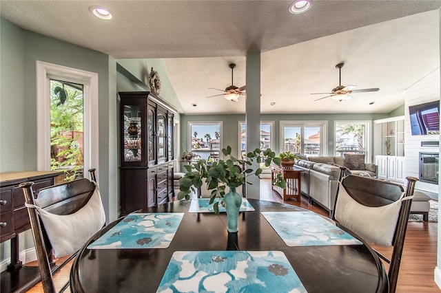 dining space featuring a textured ceiling, a large fireplace, hardwood / wood-style flooring, and vaulted ceiling