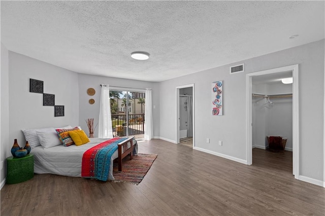 bedroom with access to exterior, dark hardwood / wood-style floors, a textured ceiling, a walk in closet, and a closet