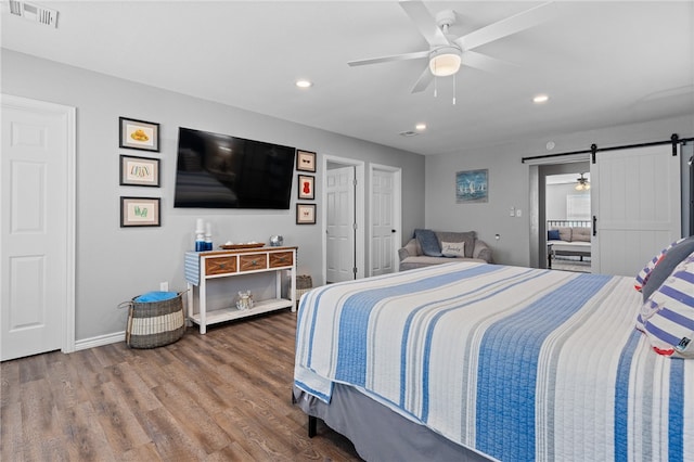 bedroom with a barn door, hardwood / wood-style floors, and ceiling fan