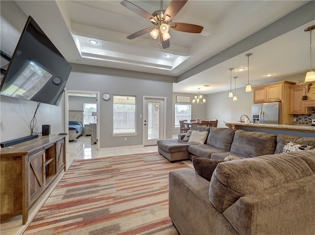 tiled living room with ceiling fan with notable chandelier and a tray ceiling