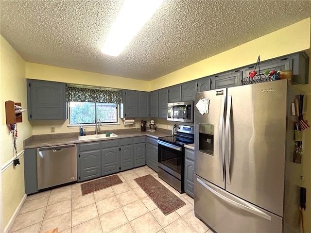 kitchen with appliances with stainless steel finishes, gray cabinetry, a textured ceiling, sink, and light tile patterned floors