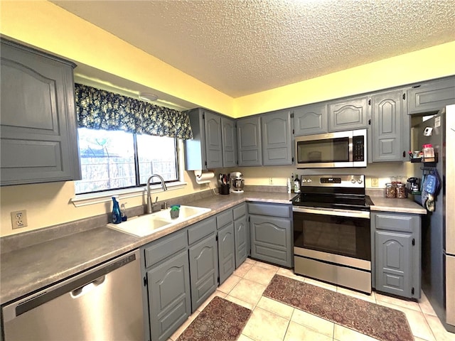 kitchen with sink, gray cabinets, light tile patterned floors, a textured ceiling, and stainless steel appliances