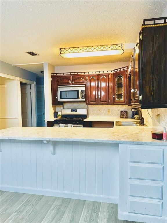 kitchen featuring backsplash, white gas range, light hardwood / wood-style flooring, and a textured ceiling