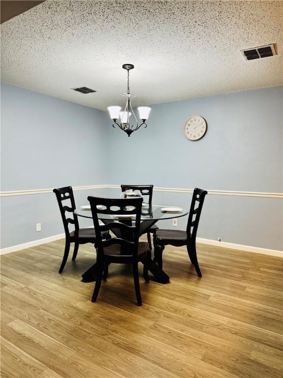 dining space with a textured ceiling, light hardwood / wood-style flooring, and a chandelier