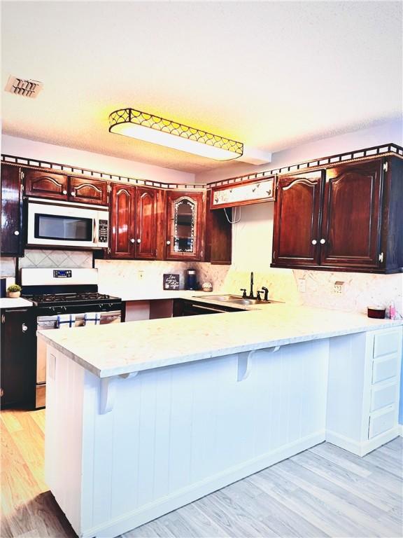 kitchen featuring light hardwood / wood-style floors, kitchen peninsula, and white range with gas cooktop