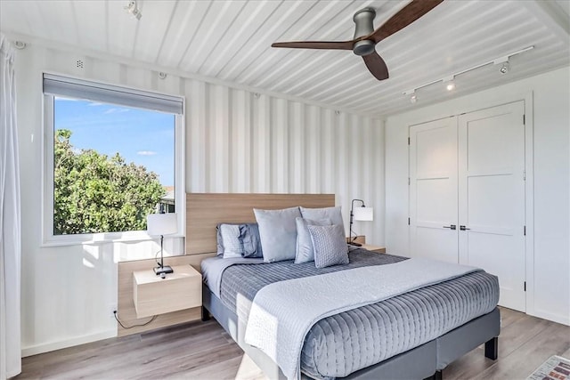 bedroom featuring ceiling fan, rail lighting, a closet, and light wood-type flooring