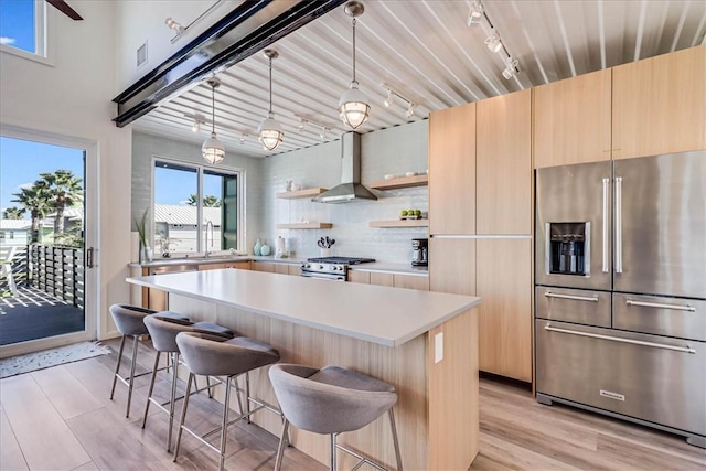 kitchen with wall chimney exhaust hood, a breakfast bar area, decorative light fixtures, a kitchen island, and stainless steel appliances