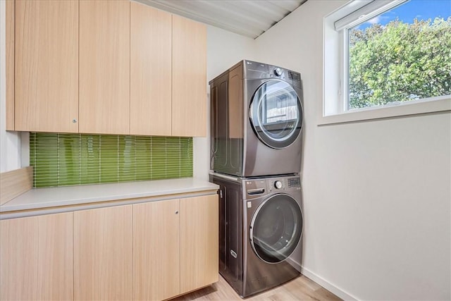 washroom with stacked washer / dryer, cabinets, and light hardwood / wood-style flooring