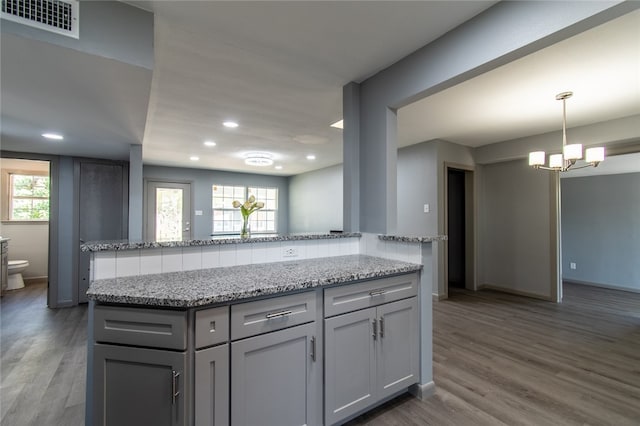 kitchen with a wealth of natural light, wood-type flooring, decorative light fixtures, and light stone counters