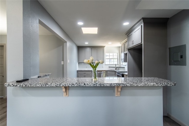 kitchen with gray cabinets, dark wood-type flooring, kitchen peninsula, and light stone counters