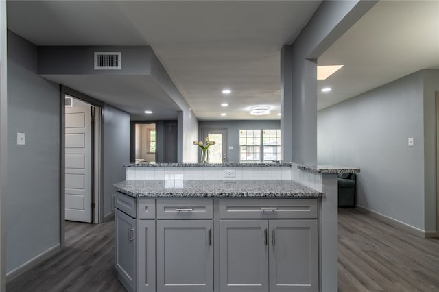 kitchen with dark wood-type flooring, kitchen peninsula, light stone counters, and gray cabinets