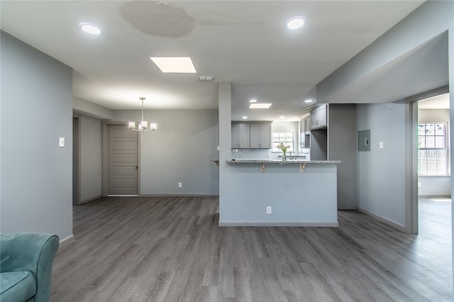 kitchen featuring kitchen peninsula, light stone countertops, decorative light fixtures, dark wood-type flooring, and gray cabinetry