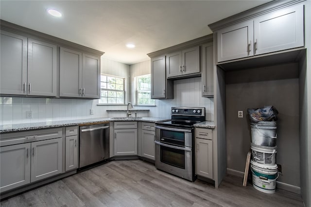 kitchen with stainless steel appliances, sink, light wood-type flooring, and light stone counters