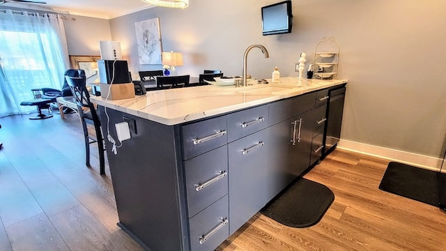 kitchen with light wood-style flooring, a peninsula, a sink, baseboards, and a kitchen bar