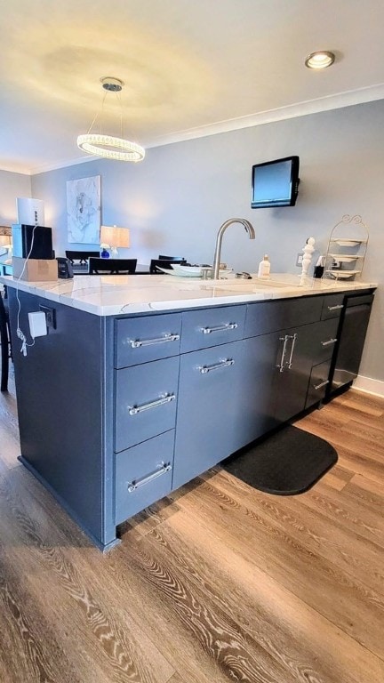 kitchen featuring light stone counters, a breakfast bar, a sink, wood finished floors, and ornamental molding