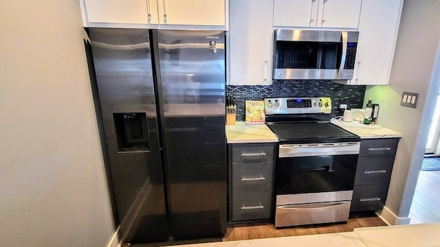 kitchen featuring tasteful backsplash, appliances with stainless steel finishes, white cabinets, wood finished floors, and baseboards