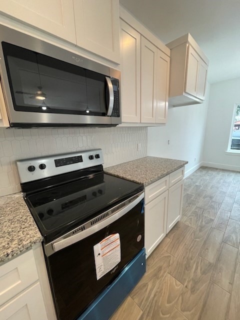 kitchen with decorative backsplash, light stone countertops, electric range oven, and white cabinets