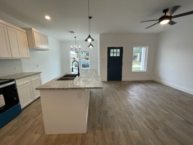 kitchen featuring pendant lighting, sink, stove, a kitchen island with sink, and light stone counters