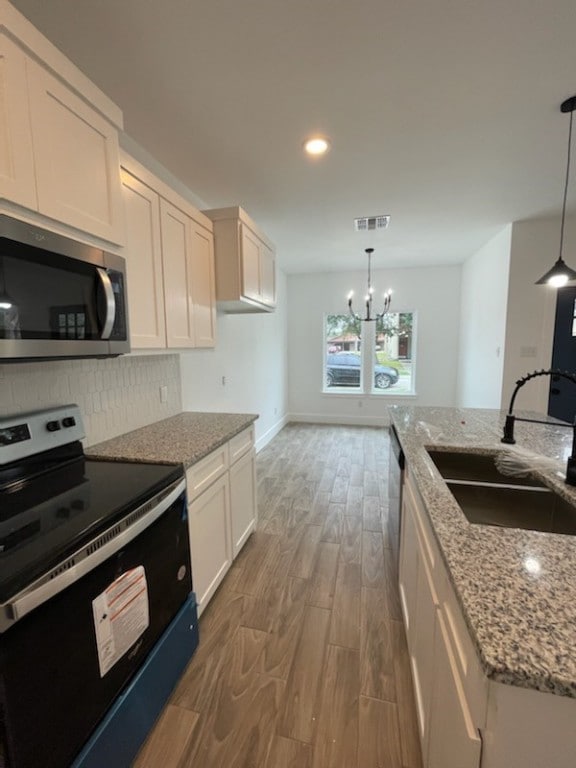 kitchen with range with electric cooktop, pendant lighting, white cabinetry, sink, and light stone countertops